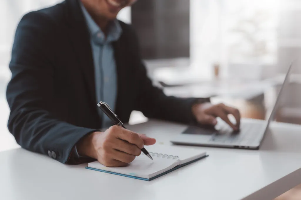 Business professional taking notes beside a laptop